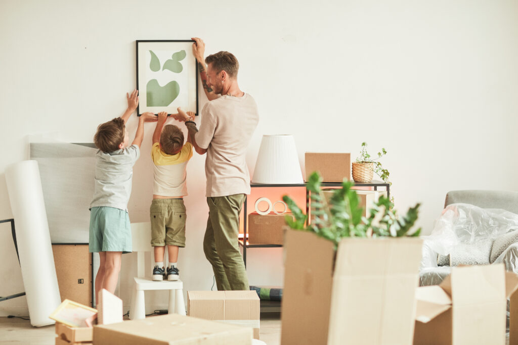 two kids and dad hanging up picture in new house